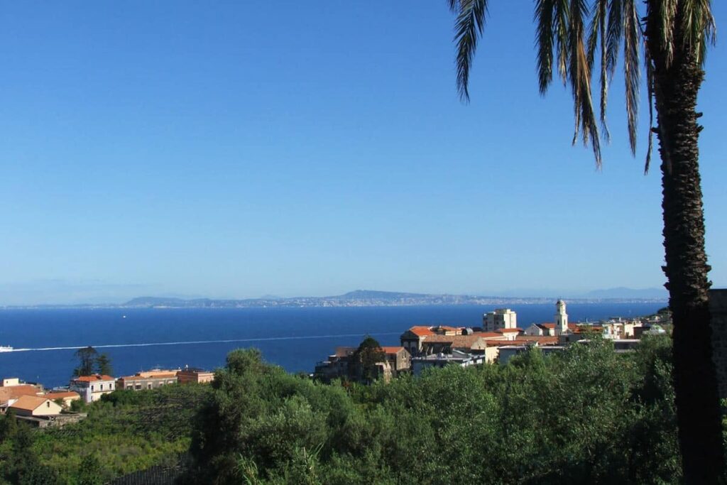 Scenic coastal view featuring lush greenery, a distant shoreline, and clear blue skies, highlighting the beauty of a Mediterranean landscape. | Only on SopranoVillas