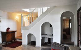 Modern interior design featuring a staircase with arched details, a cozy living area with a dark wood cabinet, and natural light illuminating the space. The color palette is predominantly white, creating a bright and airy atmosphere.