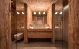 Modern bathroom design featuring natural wood elements, glass shower enclosure, and stylish lighting. The space includes a wooden vanity with dual sinks, creating a warm and inviting atmosphere.