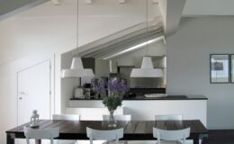 Modern kitchen and dining area featuring a wooden table with white chairs, pendant lighting, and a vase of flowers, complemented by a sleek, minimalist design.