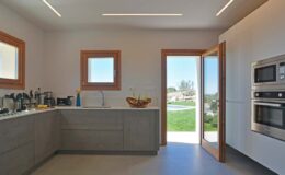 Modern kitchen interior featuring gray cabinets, stainless steel appliances, and large windows with natural light. The open door leads to a scenic outdoor view, enhancing the airy atmosphere.