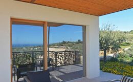 Modern balcony view with wooden ceiling, featuring a stylish railing overlooking a scenic landscape with olive trees and distant ocean views. Ideal for outdoor relaxation.