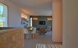 Modern open-concept living space featuring a stylish dining area, stone accent wall, and large windows allowing natural light. The decor combines minimalist design with cozy furnishings, creating a welcoming atmosphere.