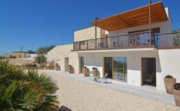 Modern two-story house with a spacious balcony, surrounded by gravel landscaping and potted plants, set against a clear blue sky. Ideal for outdoor relaxation and stylish living.