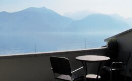 Balcony view overlooking a serene lake and misty mountains, featuring a small round table and two chairs, ideal for relaxation and enjoying nature.