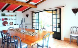 Bright and airy dining room featuring a large wooden table surrounded by stylish chairs, with a view of a garden through French doors, complemented by rustic decor and a modern aesthetic.