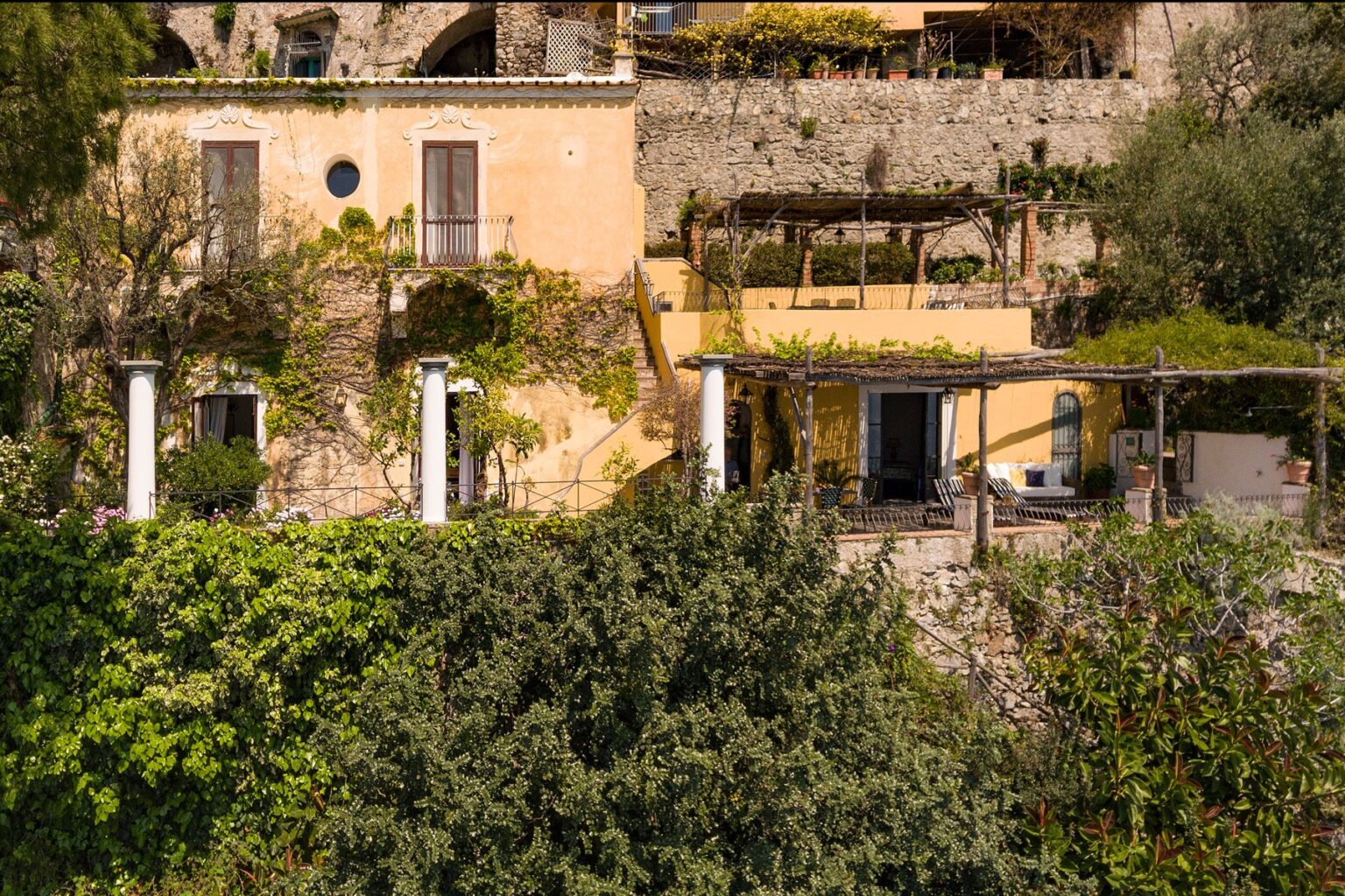 Charming hillside villa surrounded by lush greenery, featuring outdoor terraces and rustic stone architecture, ideal for a serene getaway. | Only on SopranoVillas