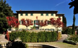 Historic villa surrounded by vibrant autumn foliage and lush greenery, showcasing a classic architectural design with large windows and a welcoming entrance. Perfect for travel and real estate enthusiasts.
