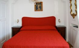 Cozy bedroom featuring a red bedspread, wooden nightstands, a chandelier, and framed artwork on the wall, creating a warm and inviting atmosphere.