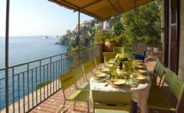 Scenic outdoor dining area overlooking the sea, featuring a beautifully set table with green chairs and a stunning coastal view.