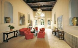 Spacious living room featuring elegant red seating, a decorative chandelier, and large windows that provide natural light, complemented by modern artwork and stylish furnishings. Ideal for interior design inspiration.