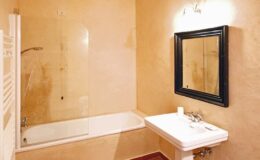 Modern bathroom featuring a glass shower enclosure, a white bathtub, a sleek sink with chrome fixtures, and a stylish black-framed mirror against a warm, textured wall. Ideal for home decor inspiration.