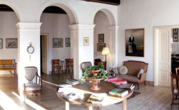 Spacious and elegantly designed living room featuring arched doorways, a round wooden coffee table with books and a decorative plant, vintage seating, and framed artwork on the walls, creating a warm and inviting atmosphere.