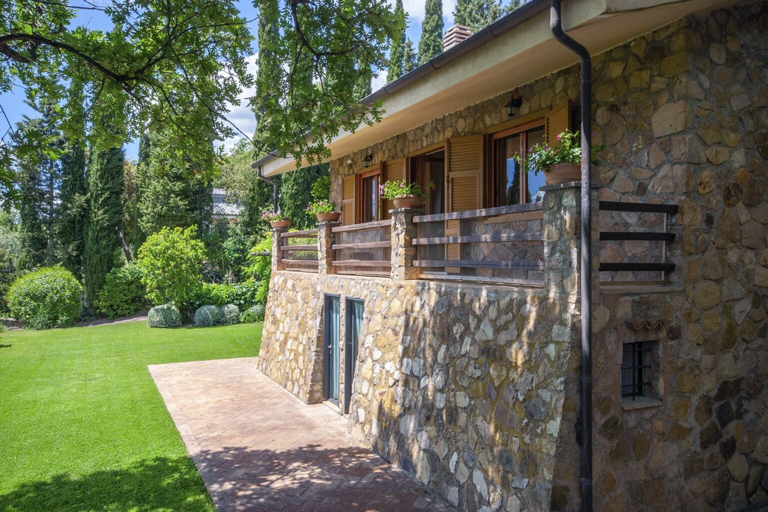 Stone house exterior with a spacious balcony, surrounded by lush greenery and a well-maintained garden. | Only on SopranoVillas