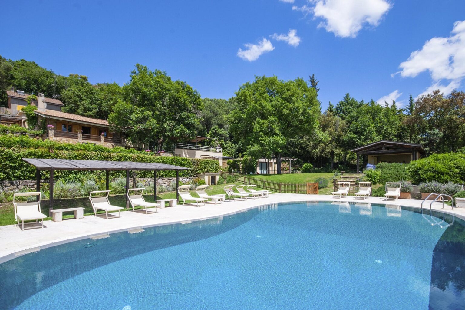 Luxury outdoor pool surrounded by lush greenery and lounge chairs, with a clear blue sky in the background, ideal for relaxation and leisure. | Only on SopranoVillas