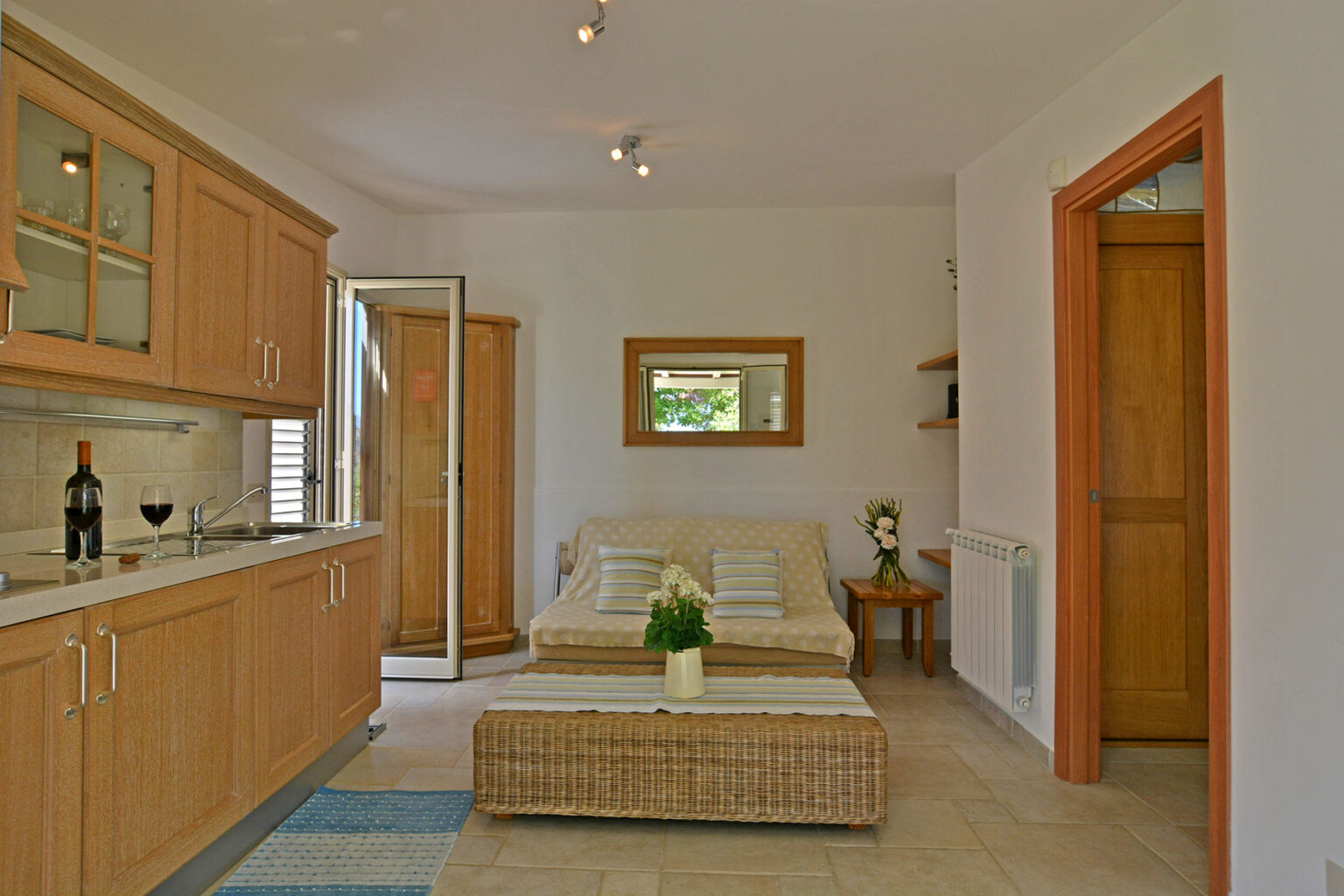 Cozy living area featuring a modern kitchen with wooden cabinets, a comfortable sofa, a coffee table, and a decorative plant, illuminated by natural light. | Only on SopranoVillas