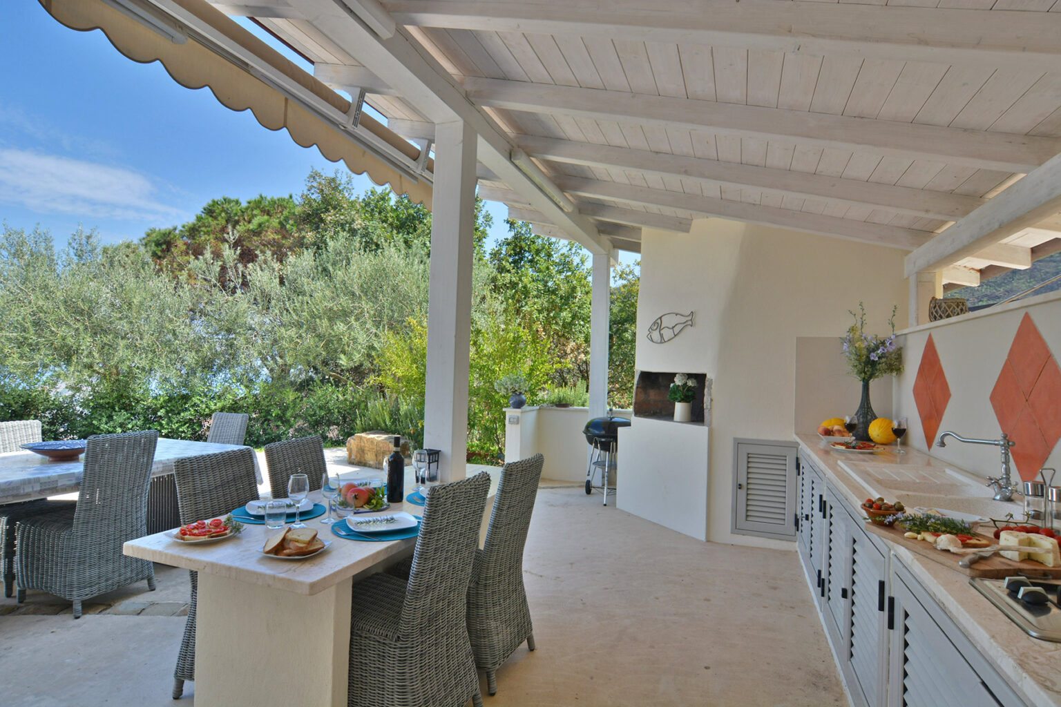 Outdoor kitchen with dining area featuring modern appliances, stylish furnishings, and a scenic view of greenery, perfect for entertaining and alfresco dining. | Only on SopranoVillas