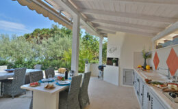 Outdoor kitchen with dining area featuring modern appliances, stylish furnishings, and a scenic view of greenery, perfect for entertaining and alfresco dining.
