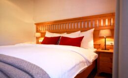 Cozy bedroom featuring a wooden bed frame with white bedding and red accent pillows, complemented by bedside lamps and a warm, inviting atmosphere.