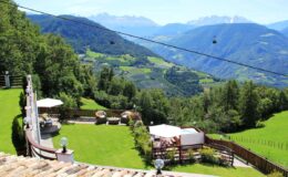 Scenic view of lush green hills and mountains in the background, featuring a well-maintained garden area with patio furniture, perfect for outdoor relaxation. The image captures the beauty of the landscape, showcasing a tranquil atmosphere ideal for nature lovers.