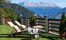 Mountain view terrace with sun loungers and a coffee table, surrounded by greenery and overlooking a scenic landscape. Ideal for relaxation in a tranquil setting.