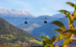 A scenic view of a cable car traversing the mountains, surrounded by lush greenery and distant peaks under a clear blue sky.