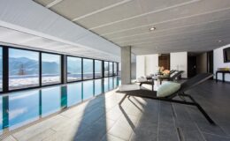Modern indoor swimming pool with panoramic mountain views, featuring sleek lounge chairs and large windows for natural light.