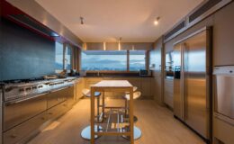 Modern kitchen with stainless steel appliances, a central island with seating, and large windows showcasing a scenic view. Ideal for contemporary home design and culinary activities.