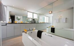 Modern bathroom featuring a freestanding white bathtub, sleek gray cabinetry, and large mirrors. Natural light floods the space, highlighting decorative accessories and a minimalist design. Ideal for showcasing contemporary interior styles.