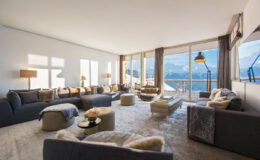 Spacious modern living room with panoramic mountain views, featuring plush sofas, a cozy rug, and large windows that invite natural light.