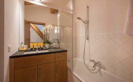 Modern bathroom featuring a sleek design with a glass shower enclosure, a bathtub, and a wooden vanity with toiletries. Natural light filters in, highlighting the clean, minimalist aesthetic.