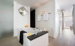 Modern bathroom featuring a sleek freestanding bathtub, elegant mirror, and soft lighting. The space is adorned with white walls and wooden flooring, creating a serene and inviting atmosphere. Fresh towels hang on the wall, and natural light streams in from a nearby window.