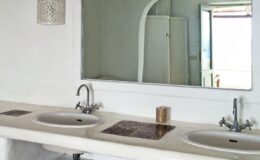 Modern bathroom with double sinks, a large mirror, and minimalist decor. Features white walls and a sleek design, enhancing the sense of space and light.