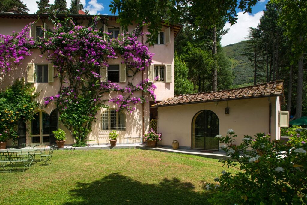Charming pink villa with blooming bougainvillea, surrounded by lush greenery and a well-maintained garden, showcasing a peaceful outdoor space in a scenic landscape. | Only on SopranoVillas