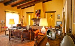 Cozy living room featuring yellow walls, wooden beams, a stone fireplace, and stylish furnishings, including lamps and decorative items, creating a warm and inviting atmosphere.