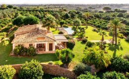 Aerial view of a charming villa surrounded by lush greenery and palm trees, featuring a swimming pool and landscaped gardens, ideal for a serene getaway.