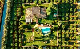Aerial view of a beautifully landscaped property featuring a spacious house surrounded by lush greenery and a swimming pool, showcasing a serene outdoor setting ideal for relaxation and leisure.