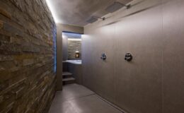 Modern bathroom interior featuring a sleek shower area with stone walls, minimalist design, and ambient lighting. The space includes dual shower heads and a stylish, contemporary aesthetic.