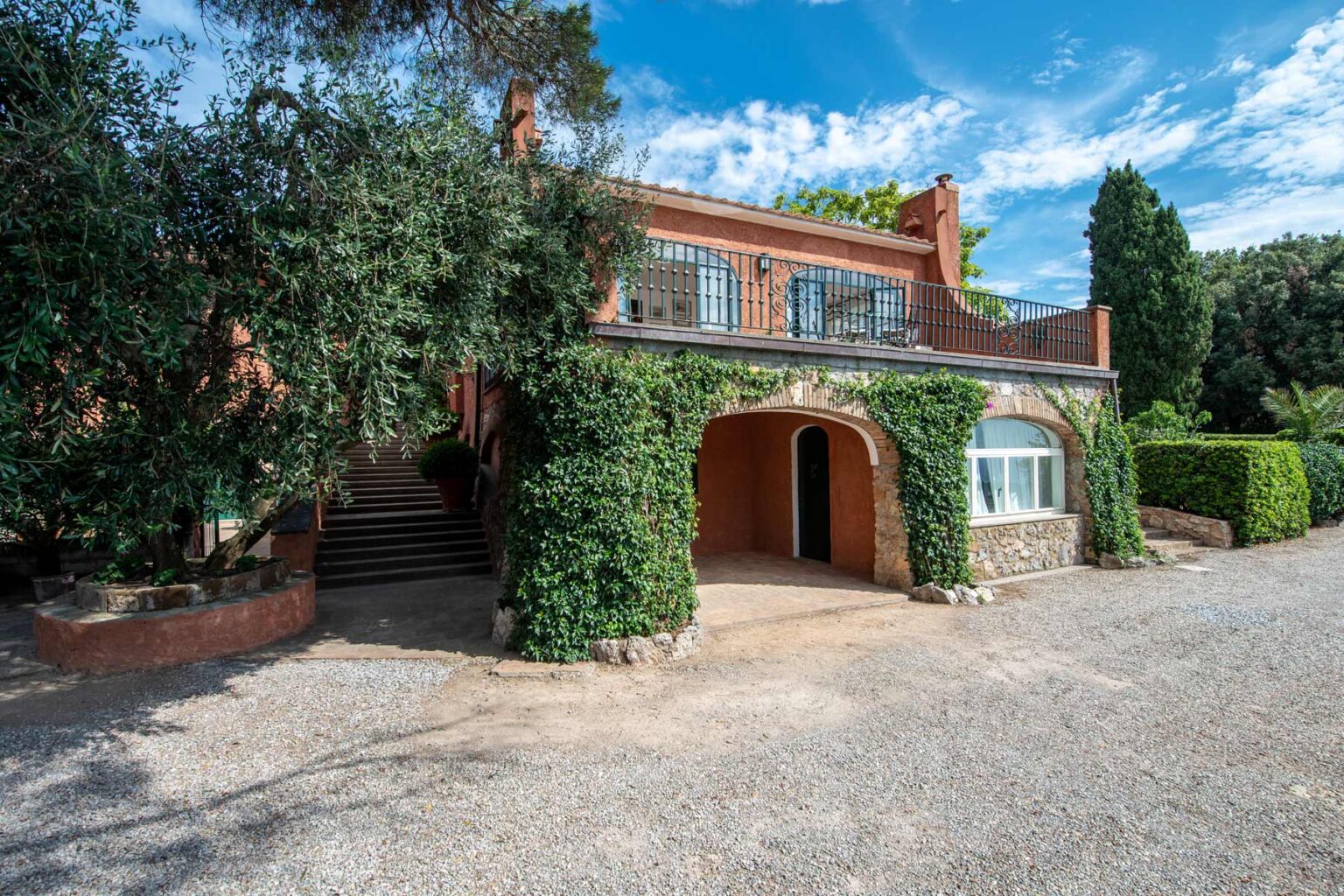 Charming two-story brick house surrounded by greenery, featuring a spacious driveway and a blue sky backdrop. Ideal for showcasing residential architecture and landscaping. | Only on SopranoVillas