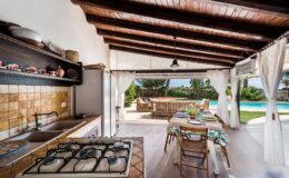 Bright and airy open-concept kitchen and dining area with wooden beams, featuring a modern gas stove, rustic decor, and a view of an outdoor patio and swimming pool. Perfect for entertaining and enjoying indoor-outdoor living.