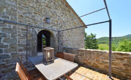Stone terrace with a table and chairs overlooking lush green hills, ideal for outdoor dining and relaxation.
