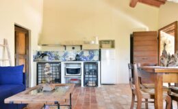 Cozy kitchen and dining area featuring a rustic design, equipped with a stove, refrigerator, and wooden dining table, complemented by blue and white tile accents and natural light.