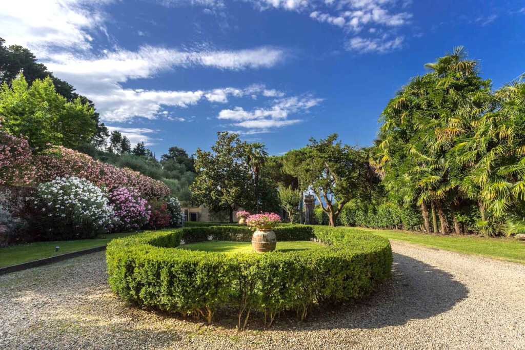 Lush garden landscape featuring a circular hedge design, vibrant flowering plants, and a serene sky, creating a tranquil outdoor setting ideal for relaxation and gardening enthusiasts. | Only on SopranoVillas