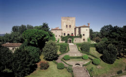 Historic castle surrounded by lush greenery and manicured gardens under a clear blue sky. The architectural features include a tall tower and stone walls, showcasing medieval design. Ideal for travel enthusiasts and history lovers.