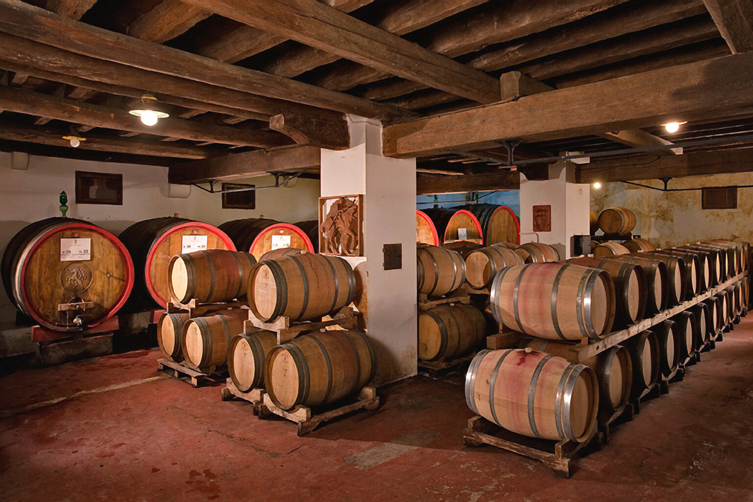 Wine cellar interior featuring wooden barrels stacked neatly on racks, with a rustic wooden ceiling and soft lighting, creating an atmosphere ideal for aging wine. | Only on SopranoVillas