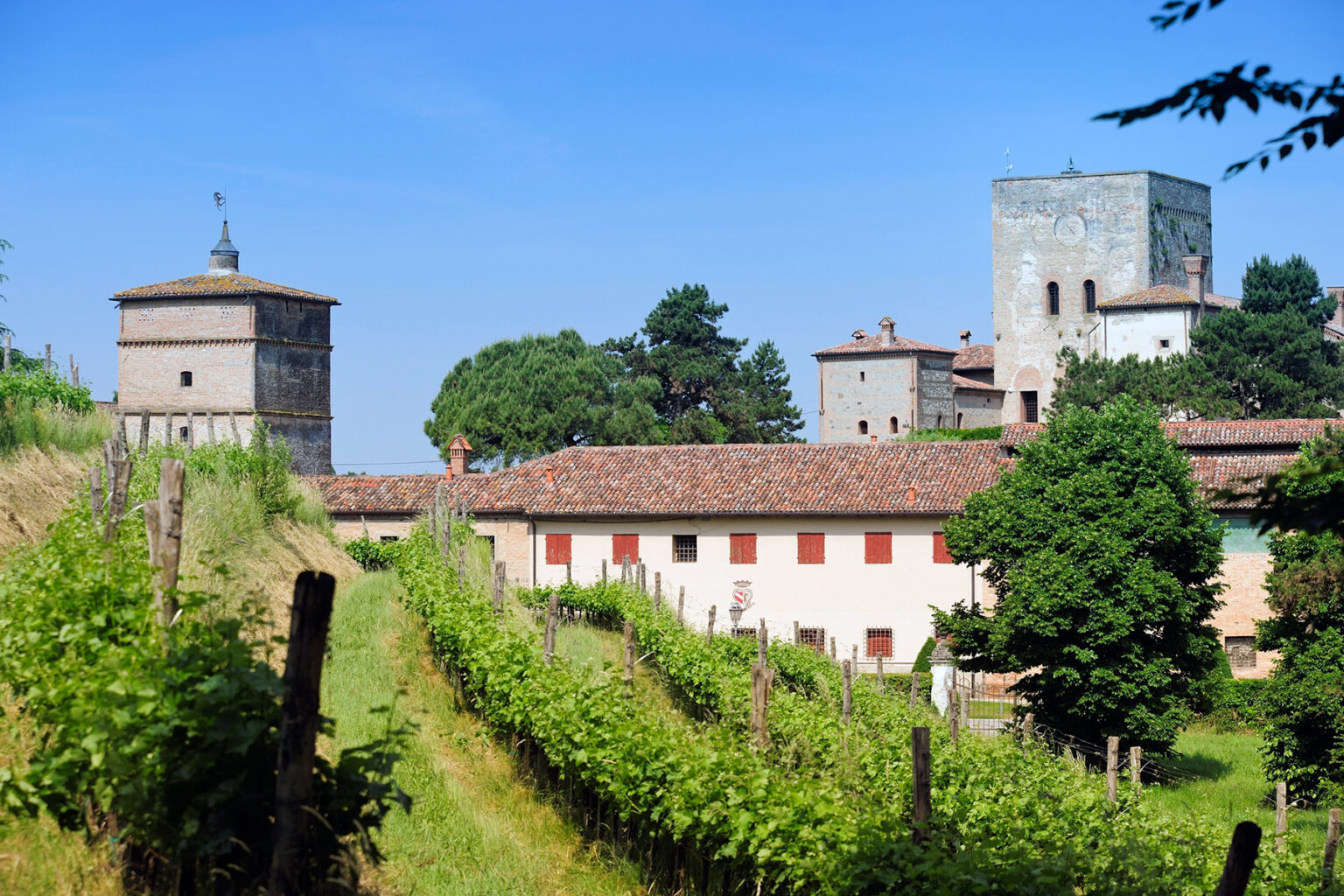 Historic village landscape featuring a vineyard, traditional buildings, and ancient towers under a clear blue sky. | Only on SopranoVillas