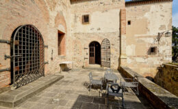 Historic castle courtyard featuring stone walls, arched doorways, and wrought iron gates, with a small table and chairs for outdoor seating. Ideal for showcasing medieval architecture and outdoor dining spaces.