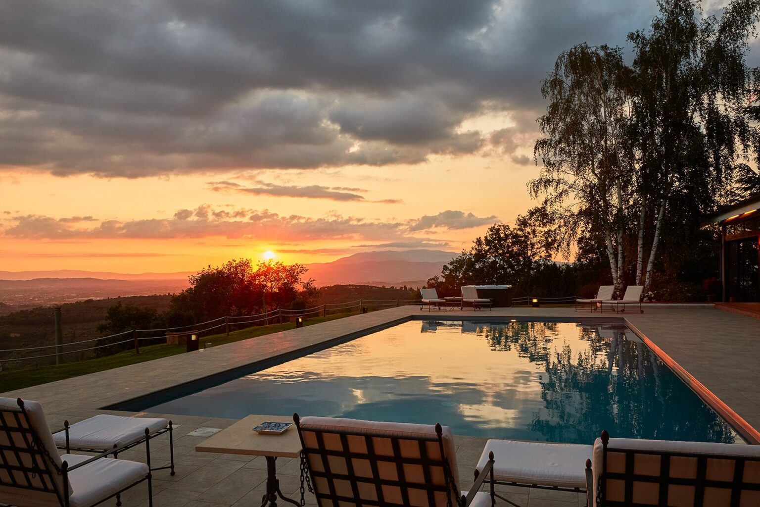 Luxurious outdoor pool area at sunset, featuring comfortable lounge chairs, scenic views of rolling hills, and a tranquil atmosphere, perfect for relaxation and leisure. | Only on SopranoVillas