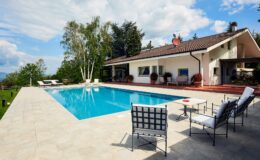 Modern villa with a swimming pool, surrounded by greenery, featuring outdoor seating and a sunny terrace. Ideal for relaxation and leisure activities.