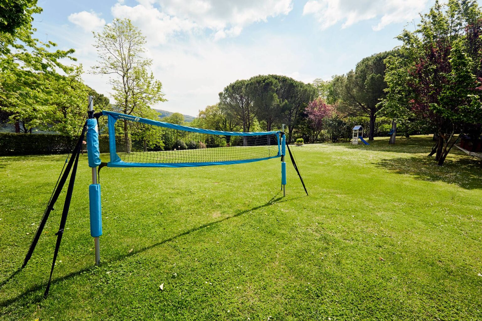 Outdoor volleyball court set up in a grassy park, surrounded by trees and a clear blue sky, ideal for recreational sports and outdoor activities. | Only on SopranoVillas